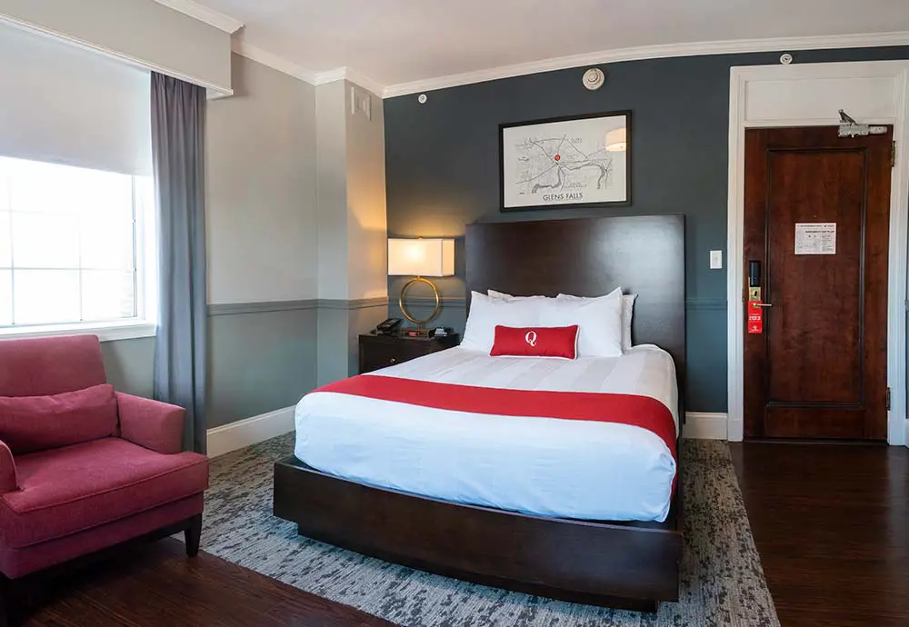 queen bed in modern styled hotel room with red chair